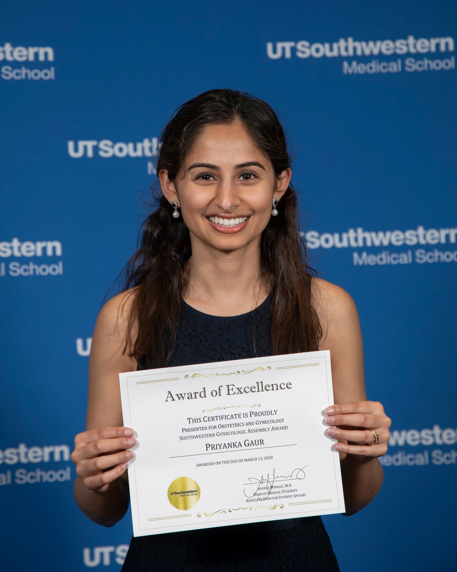 Priyanks Gaur holding The Southwestern Gynecologic Assembly award wearing a black dress and small earrings