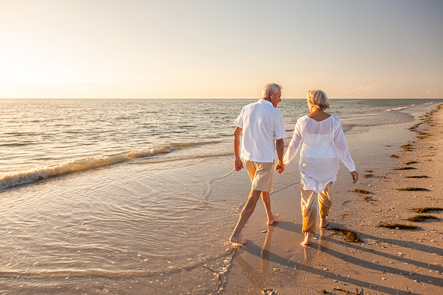 Happy Senior Old Retired Couple Walking Holding Hands on Beach a